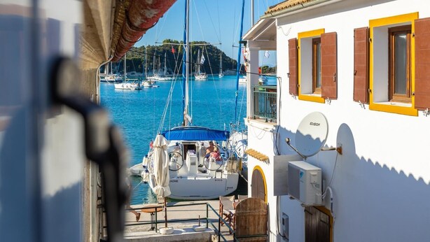 A marina with boats docked, a white building with yellow shutters, and a clear view of the water. - Flora Maisonettes 1 - Two Bedroom House, Sleeps 4 (Lakka)