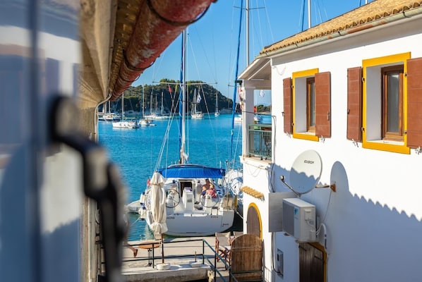 A marina with boats docked, a white building with yellow shutters, and a clear view of the water.