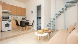A compact apartment with a kitchenette, a dining area, a living room with a sofa, and a blue staircase. - Flora Maisonettes 1 - Two Bedroom House, Sleeps 4 (Lakka)