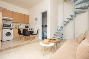 A compact apartment with a kitchenette, a dining area, a living room with a sofa, and a blue staircase.