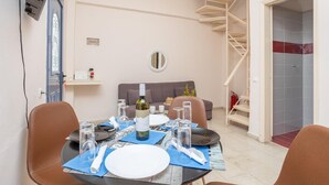 A dining area with a table set for two, a sofa, a spiral staircase, and a tiled shower area.