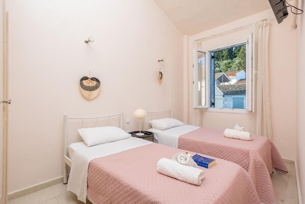 Une chambre avec deux lits, une fenêtre donnant sur un beau paysage, un décor mural en forme de cœur et une lampe.