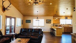 A spacious living room with a wooden ceiling, a chandelier, leather sofas, and a dining area with wooden cabinets. - BearLuckLodge! Amazing Cabin-Hot Tub, Views, Game Room/Arcade, Location, Peloton (Ruidoso)