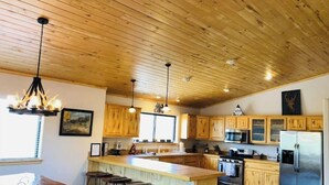 A spacious kitchen with wooden cabinets, a central island with stools, stainless steel appliances, and pendant lighting. - BearLuckLodge! Amazing Cabin-Hot Tub, Views, Game Room/Arcade, Location, Peloton (Ruidoso)