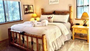 A bedroom with a wooden bed, white bedding, a bedside table with a lamp, and a window with blinds. - BearLuckLodge! Amazing Cabin-Hot Tub, Views, Game Room/Arcade, Location, Peloton (Ruidoso)
