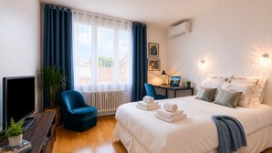 Hotellihuone, jossa on sänky, työpöytä kannettavalla tietokoneella, tuoli, televisio ja ikkuna, jossa on verhot.