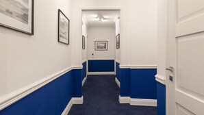 A hallway with white and blue wainscoting, framed pictures on the walls, and a carpeted floor.