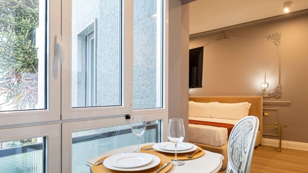 A modern bedroom with a large window, a bed, and a dining area set up with plates and glasses.