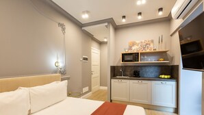 A modern hotel room with a large bed, a kitchenette, and a bathroom visible through an open door.