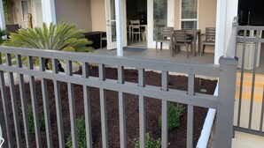 Un espace extérieur abrité, doté d’une table et de chaises de patio, d’un petit jardin avec des plantes et d’une rambarde blanche.