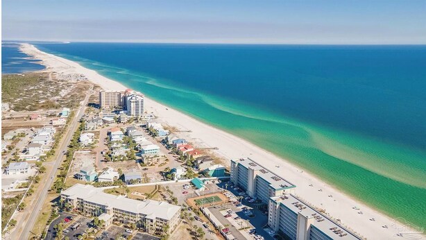 Une vue aérienne d’une zone côtière avec une plage, des bâtiments et un océan bleu limpide.