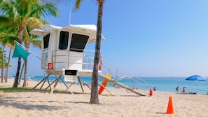 Una torre de salvavidas con un letrero del número 9, palmeras y gente en la playa al fondo.