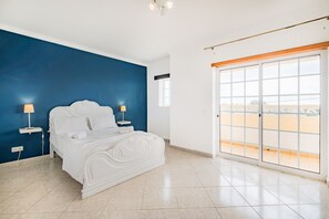 Une chambre avec un grand lit, deux lampes de chevet, une vue sur le désert grâce à une porte coulissante, et un mur d’accent bleu.