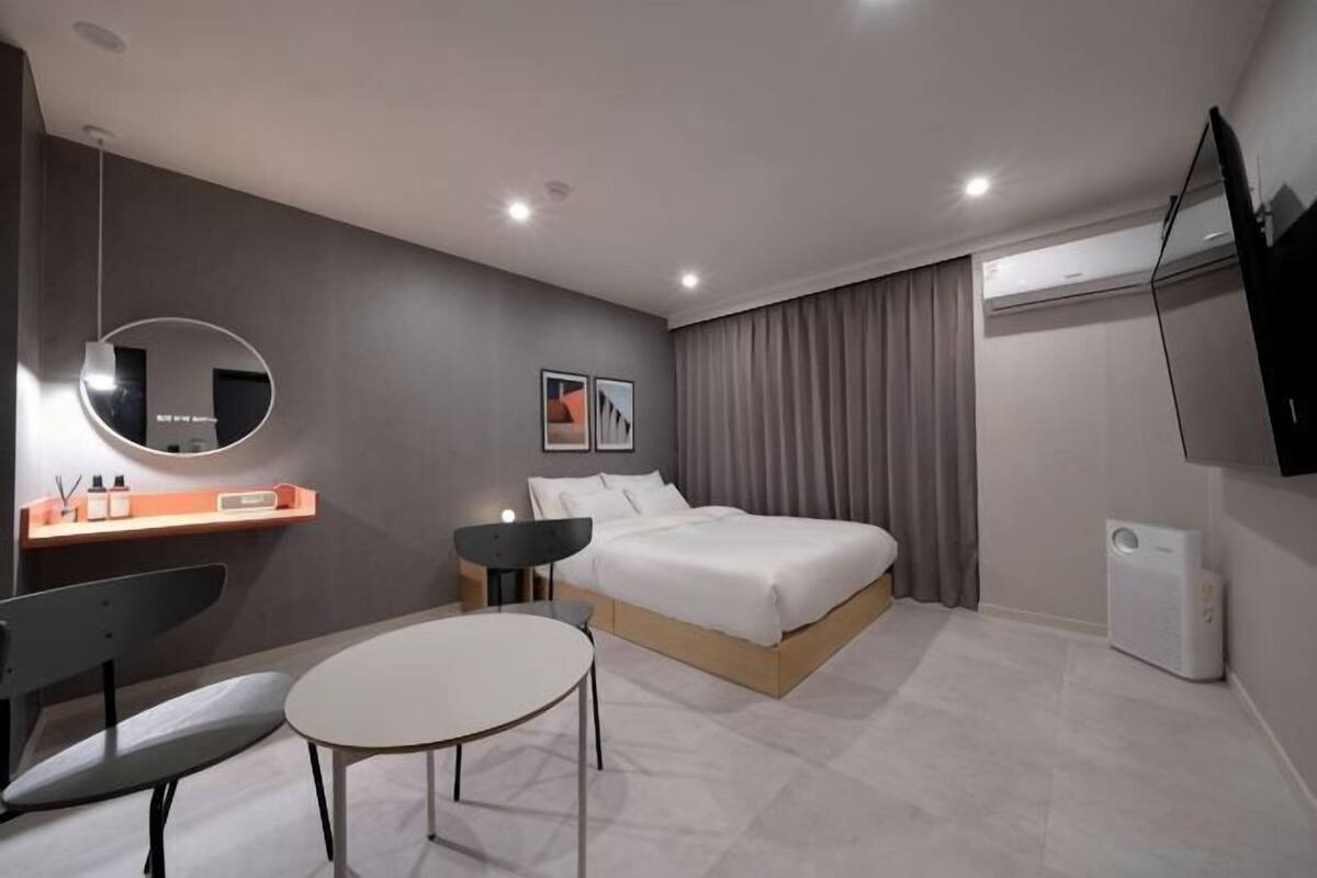 A modern hotel room with a bed, bedside table, chair, and a small table.