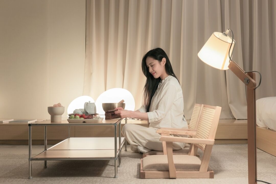 A room with a wooden chair, a small table with bowls, and a floor lamp.