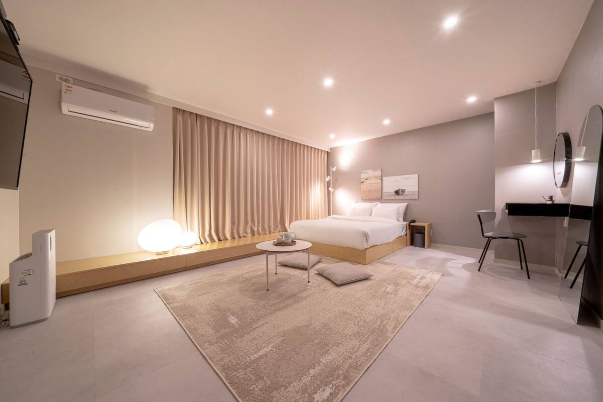A modern bedroom with a bed, bedside table, lamp, and air conditioning unit.