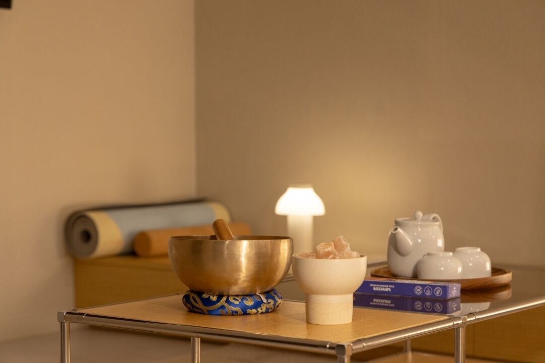 Un espacio para la meditación con un gong, un cuenco, un libro y un juego de té sobre una mesa.