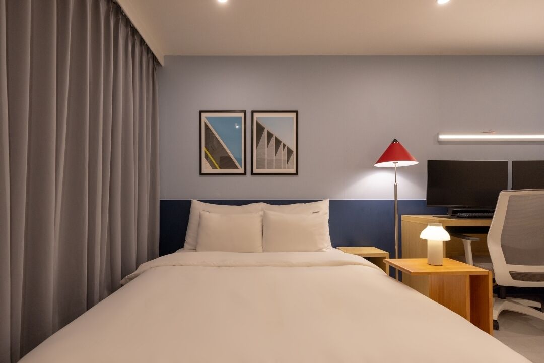 A hotel room with a bed, a desk, a chair, a TV, and two framed pictures on the wall.