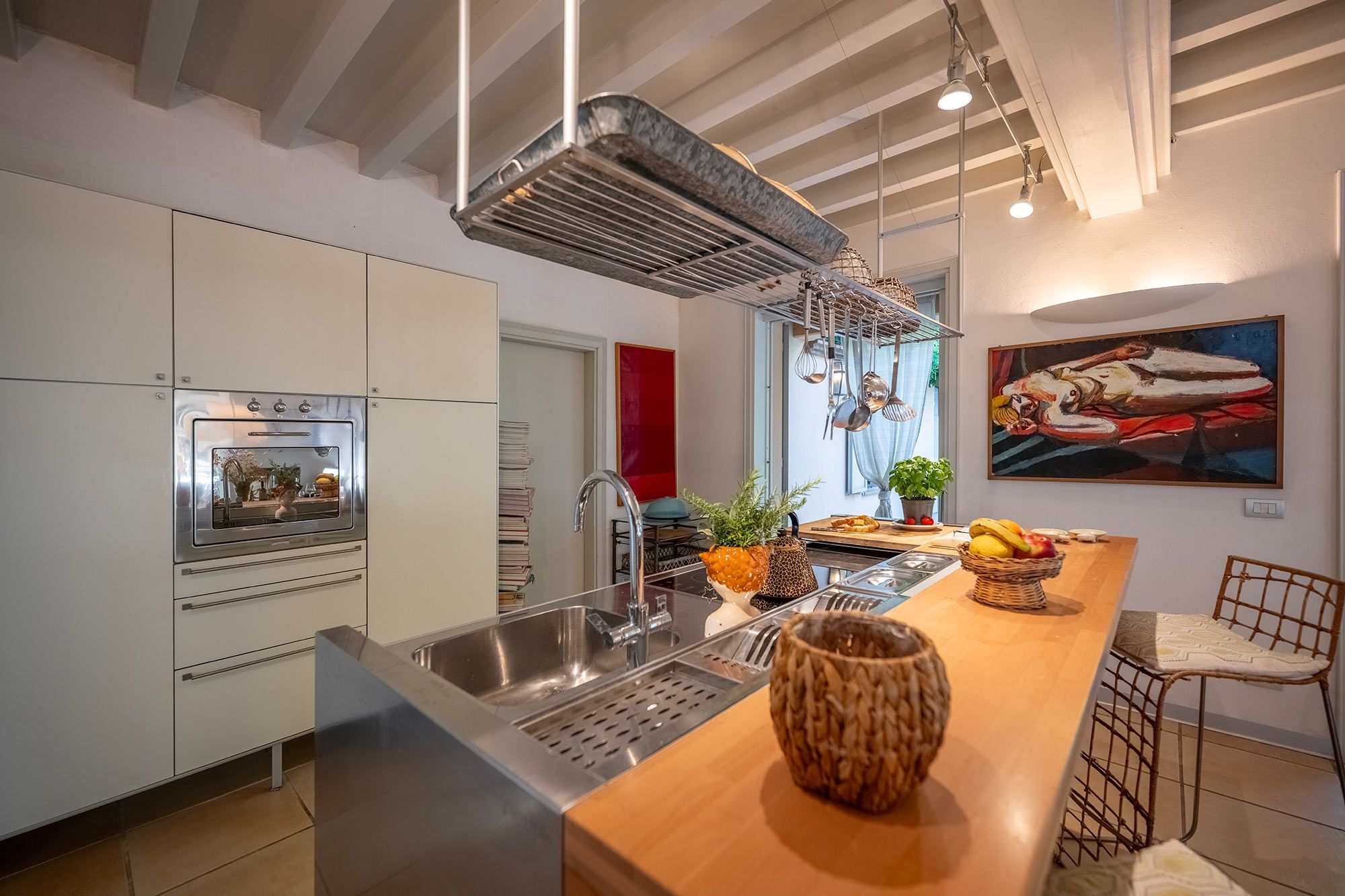 A modern kitchen with a built-in oven, stainless steel sink, and a wooden island with a woven bowl.