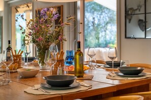 Una mesa de comedor dispuesta con platos, tazones, copas de vino y una botella de vino, con un jarrón de flores en el centro.