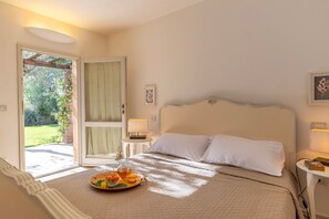 Un dormitorio con cama, una mesita de noche, una bandeja con frutas y un vaso de agua, y una puerta que da a un jardín.
