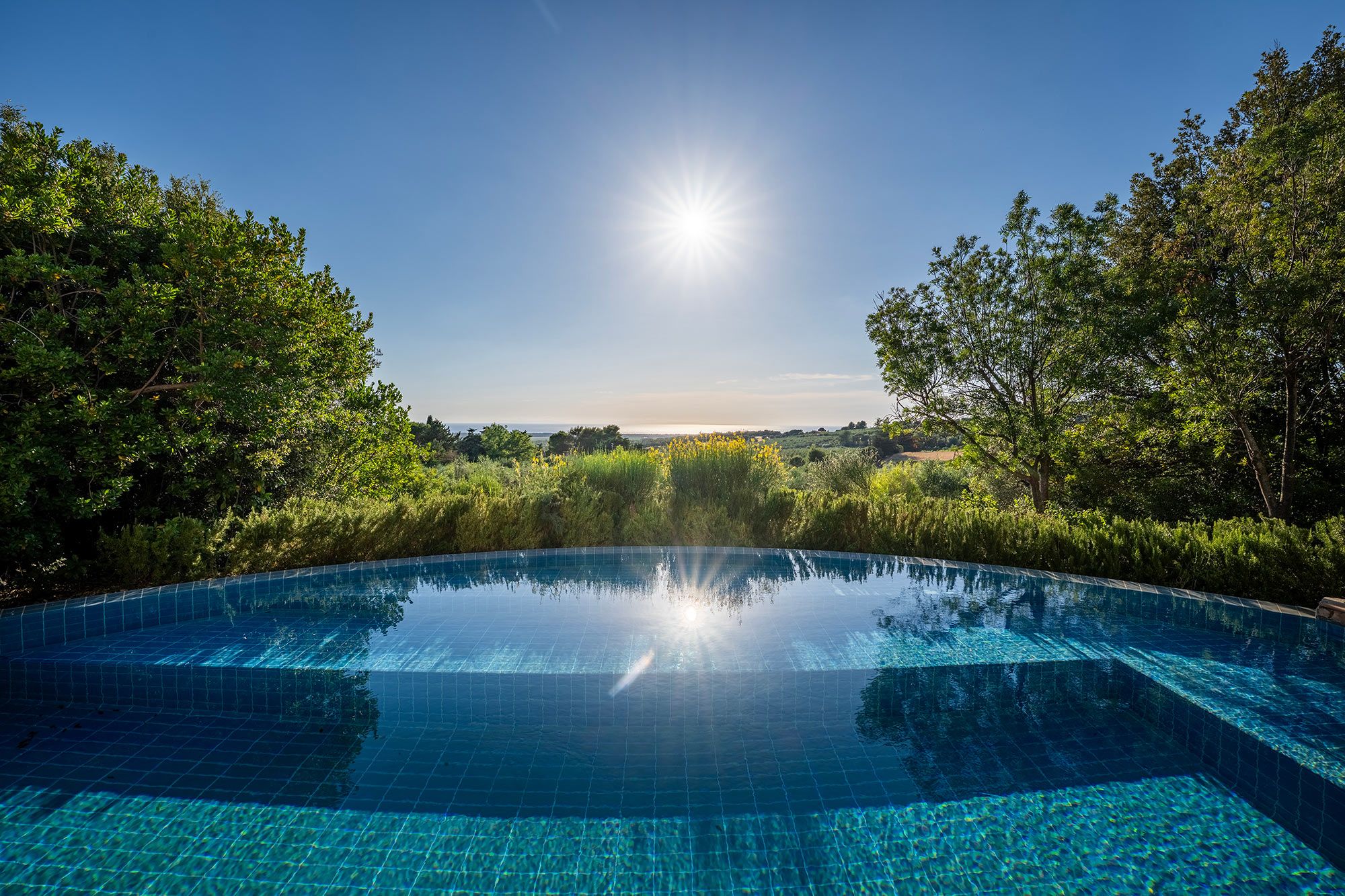 Ein klares, blaues Schwimmbecken, umgeben von üppiger Vegetation und Bäumen.