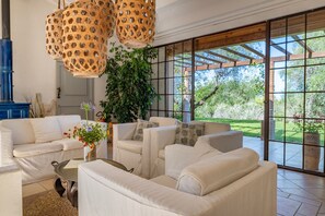 Un vaste espace de vie comprenant un canapé blanc, une table basse et une grande fenêtre donnant sur un paysage verdoyant.