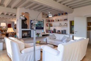 Una sala de estar moderna con chimenea, sofás blancos, un televisor y una estantería.