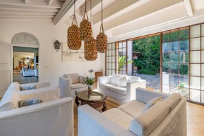 A spacious living room with a large window, white sofas, a coffee table, and hanging wicker lamps.