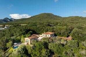 Una villa con piscina rodeada de abundante vegetación y colinas al fondo.