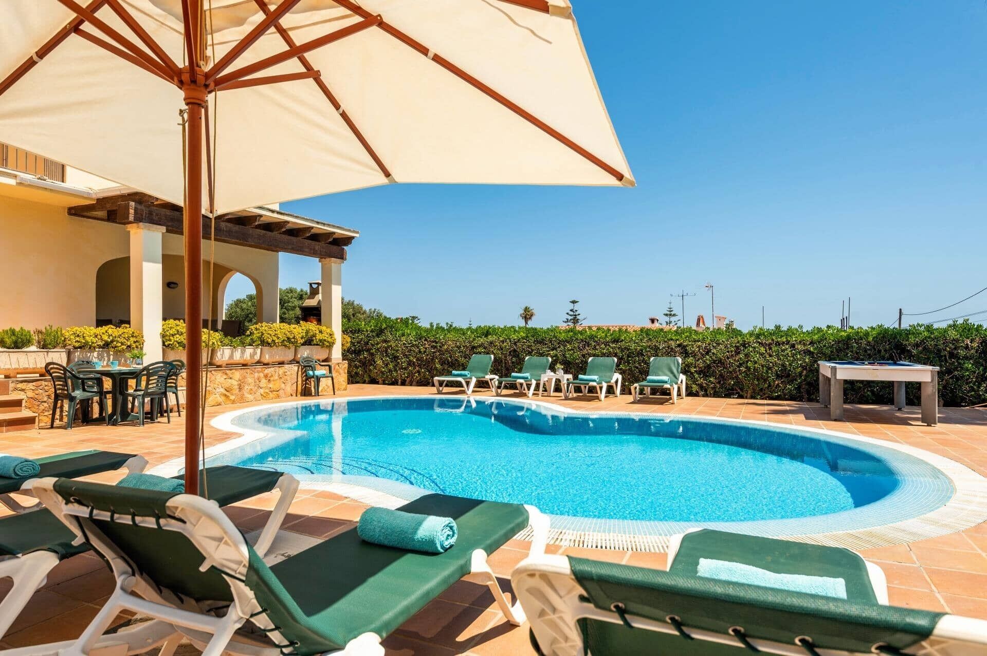 A pool area with lounge chairs, a table, and an umbrella.