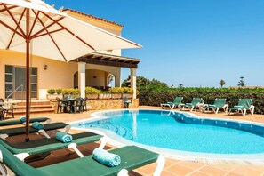 Un espace piscine avec des chaises longues et une pergola.