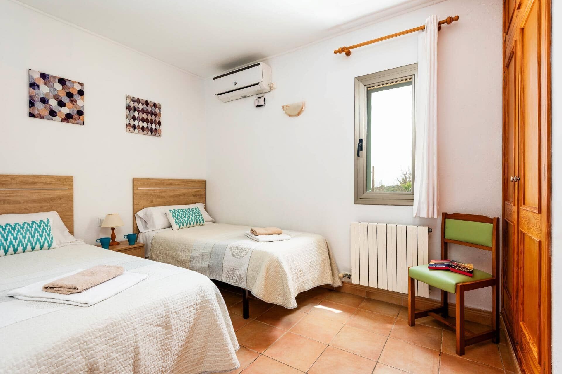 A bedroom with two beds, a radiator, a window with curtains, and a chair.
