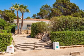 A villa with a stone wall, palm trees, and a hedge.