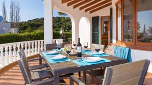 A table set for four with wine glasses, plates, and a bottle of wine, overlooking a lush garden and hills. - Villa Lavanda by Villa Plus (Sant Tomas)