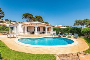 A poolside area with a pool, lounge chairs, and a building with arches.