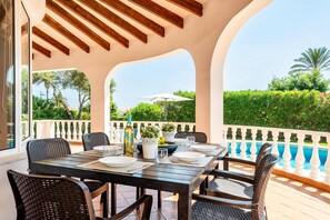 An outdoor dining area with a table set for four, surrounded by wicker chairs, overlooking a swimming pool and lush greenery.