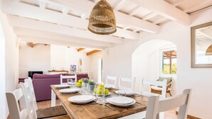 A dining area with a wooden table set for four, white chairs, and a woven pendant light. - Villa Mas Alta by Villa Plus (Ferreries)