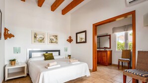 Une chambre à coucher comprenant un lit, des tables de chevet, une chaise, une salle de bain avec un miroir et des œuvres d’art accrochées aux murs.