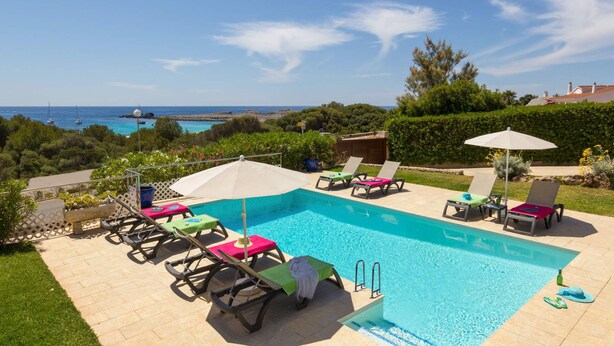 Un espace piscine agrémenté de chaises longues et de parasols, entouré de verdure et offrant une vue sur la mer.