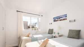 A bedroom with two beds, a window with curtains, a painting, and a nightstand with a lamp.
