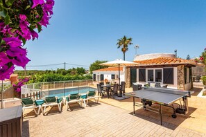 A poolside area with lounge chairs, a ping pong table, and a building with a tiled roof.