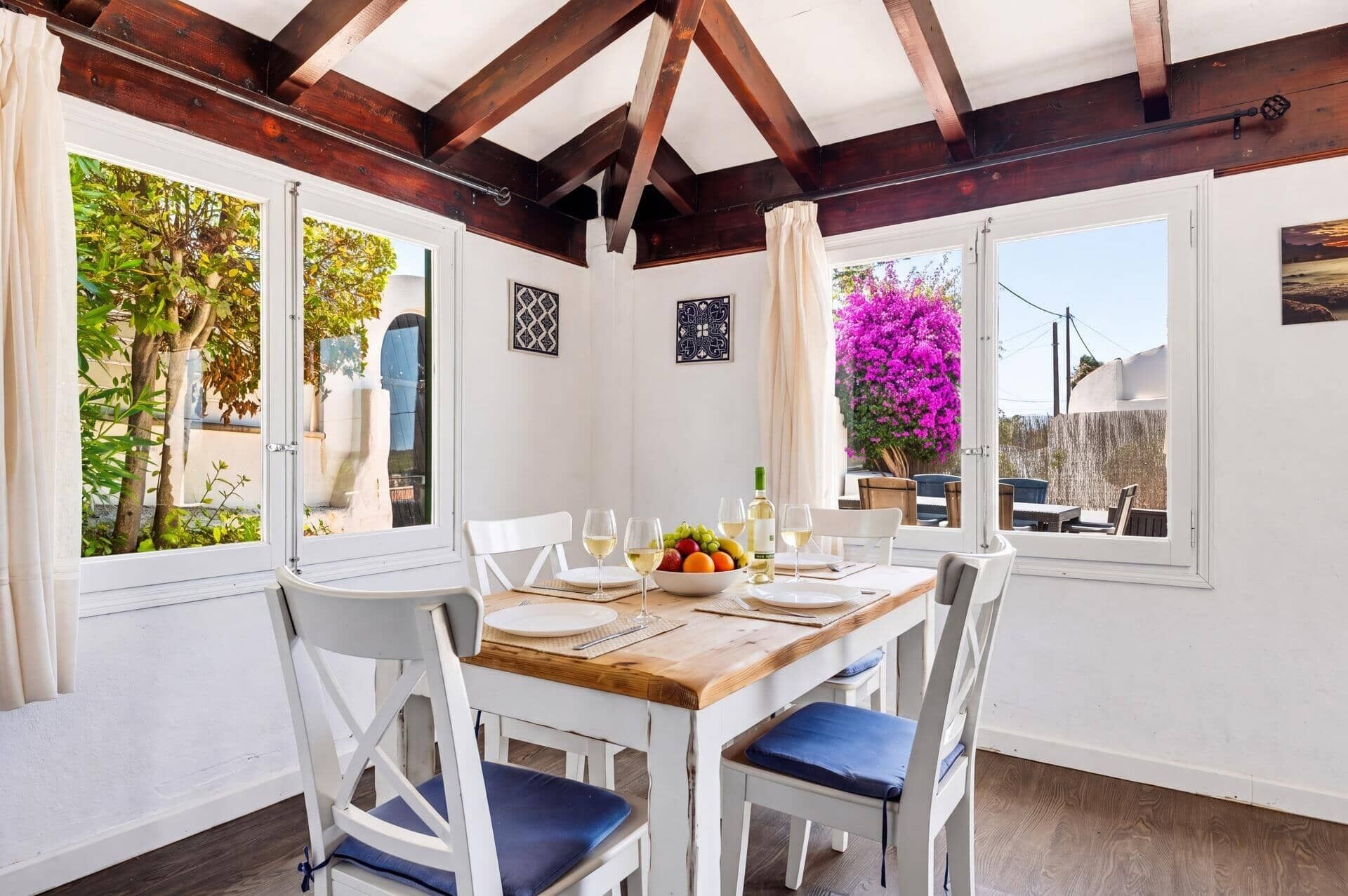 A dining area with a wooden table, white chairs, and a view of the outdoors.