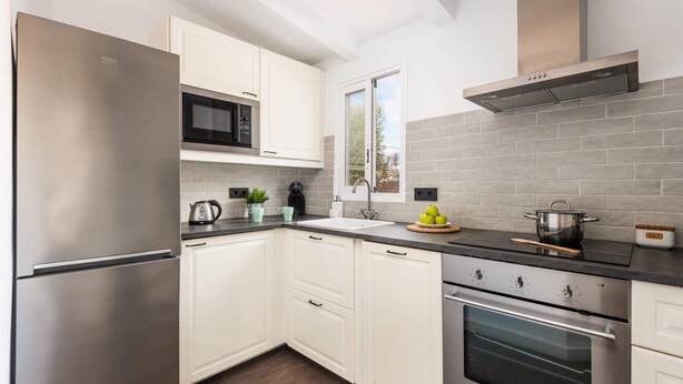 A modern kitchen with white cabinets, stainless steel appliances, and grey tiled backsplash.