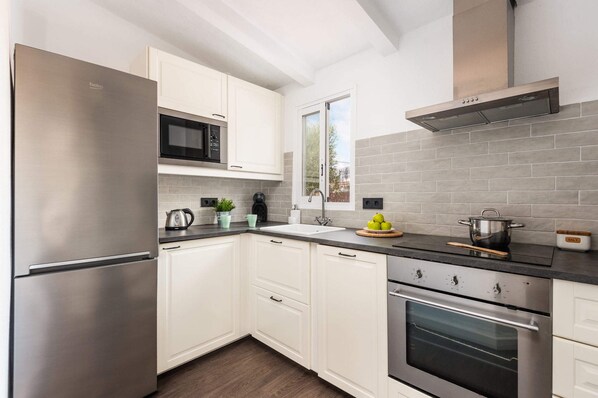 A modern kitchen with white cabinets, stainless steel appliances, and grey tiled backsplash.