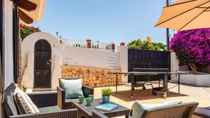 An outdoor patio with wicker furniture, a barbecue grill, and a stone wall.