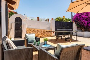 An outdoor patio with wicker furniture, a barbecue grill, and a stone wall.