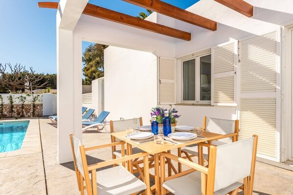 A poolside dining area with wooden furniture and a table set for two.