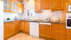 Een keuken met houten kastjes, een vaatwasser, een fornuis en een raam met gordijnen.