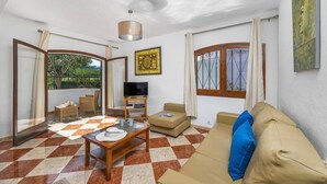 Una sala de estar con piso a cuadros, un sofá, un televisor, una mesa de comedor y un balcón con vistas.